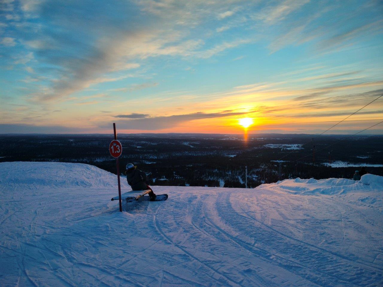 Salla Sallatunturi lumilautailija istuu penkillä, auringonlasku