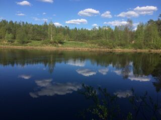 Vastarannan metsä ja lähes pilvetön taivas heijastuvat joen tyyneen pintaan.